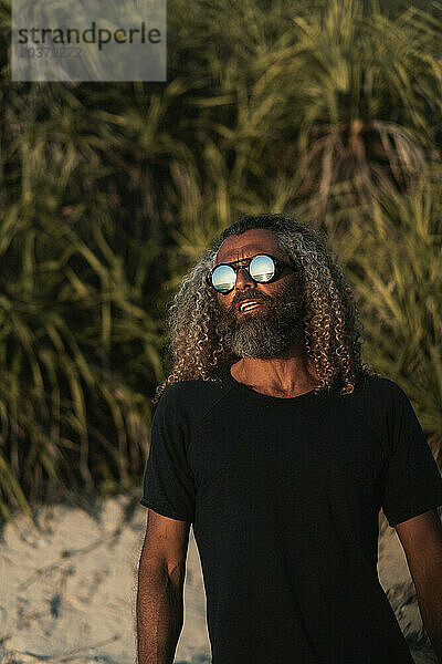 Arabischer Mann  lockiges Haar  Steampunk-Sonnenbrille entspannt am Strand.