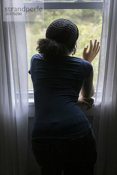 From behind  biracial teen girl looks out a window