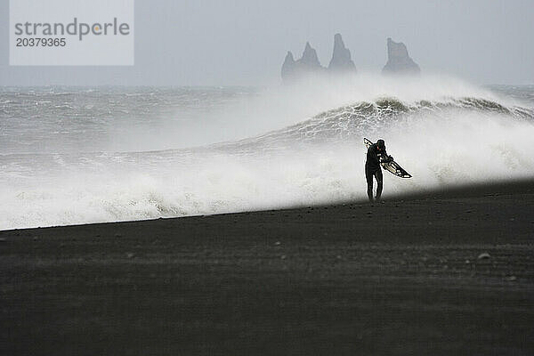 Wintersurfer geht den windigen Strand hinauf