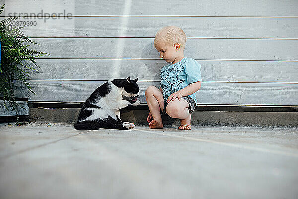 Weitwinkelaufnahme eines Kleinkindes und einer Katze  die im Sommer zusammen draußen sitzen.