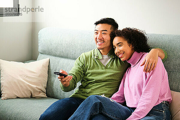 Multiethnisches Paar lächelt und schaut gemeinsam auf dem Sofa Fernsehen  Film oder Film.