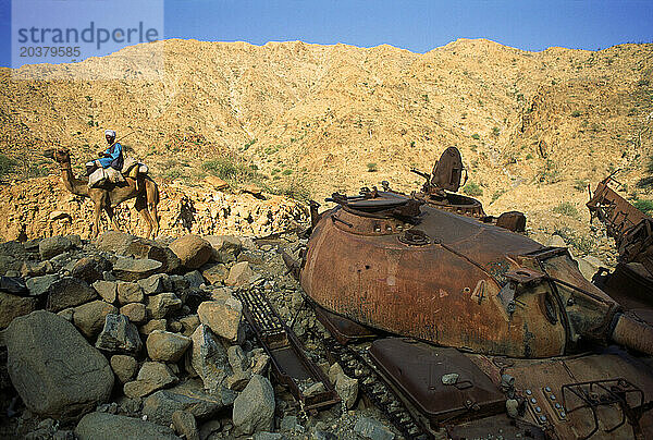 Mann reitet auf einem Kamel an einem zerstörten Panzer der äthiopischen Armee vorbei.