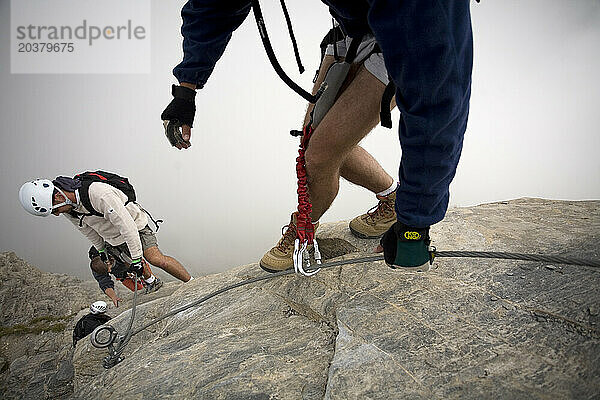 Vier Personen klettern den Felsen hinunter  während sie in den französischen Alpen den Klettersteigsport ausüben.