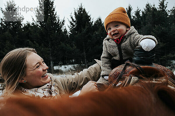 Mutter hält glücklich ihren kleinen Jungen bei seinem Abenteuer zu Pferd