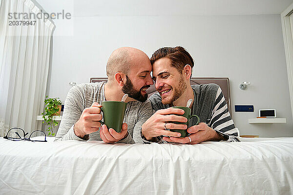 Verliebtes homosexuelles Paar trinkt gemeinsam Kaffee im Bett.