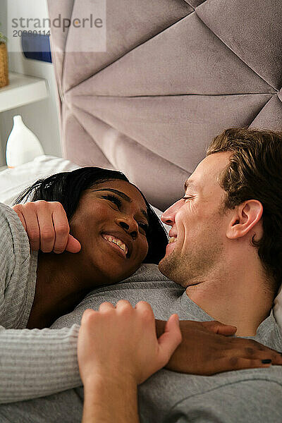 Multiethnisches verliebtes Paar umarmt sich und liegt auf dem Bett.