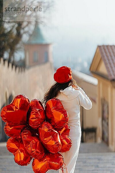 Glückliche junge Frau mit Heliumballons mit rotem Herz in Prag