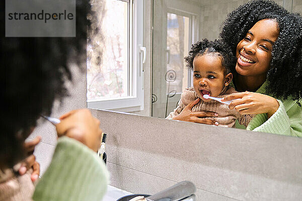 Kubanische Mutter putzt ihrer kleinen Tochter im Badezimmer die Zähne.