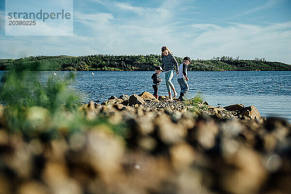 Niedrige  weite Sicht auf drei Kinder  die am felsigen Ufer des Sees spielen.