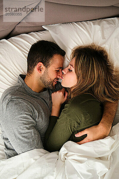 Draufsicht auf ein spanisches Paar  das sich in einem Bett verliebt küsst.