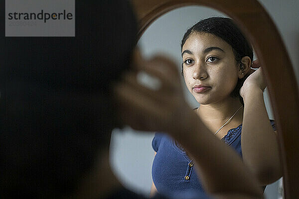 Ein gemischtrassiges Teenager-Mädchen betrachtet sich selbst kritisch im Spiegel