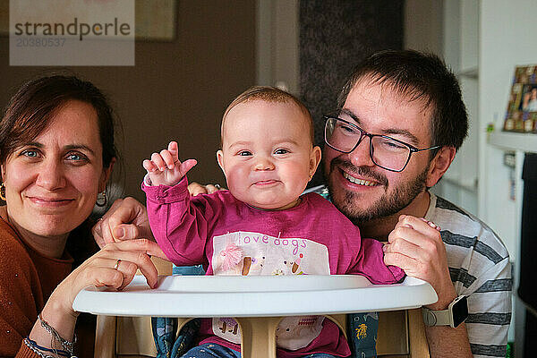 Glückliche Eltern lächeln und ein 6 Monate altes Mädchen bläst Himbeeren.