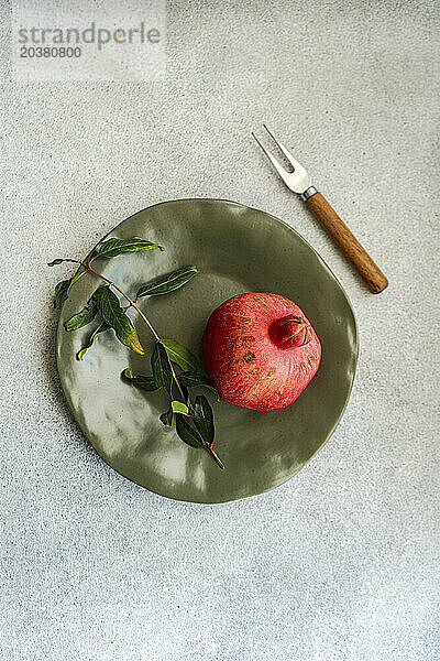 Reifer Granatapfel mit Blättern auf Teller