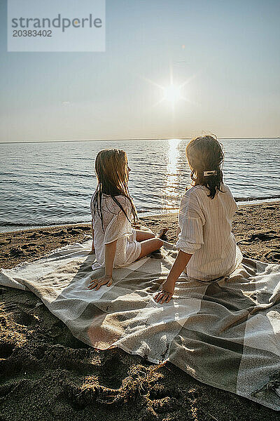 Mother and daughter sitting on blanket at beach