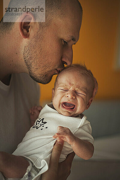 Father kissing crying baby boy at home