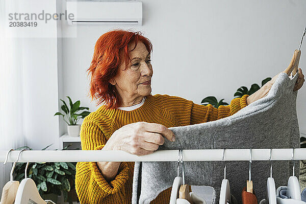 Retired senior woman choosing sweater from clothes rack at home