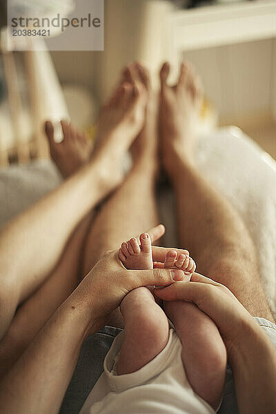 Hands of man holding baby son's feet near woman at home