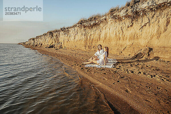 Mother and daughter spending leisure time sitting on shore at beach