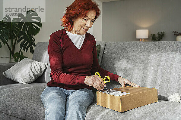 Senior woman unpacking package sitting on sofa at home