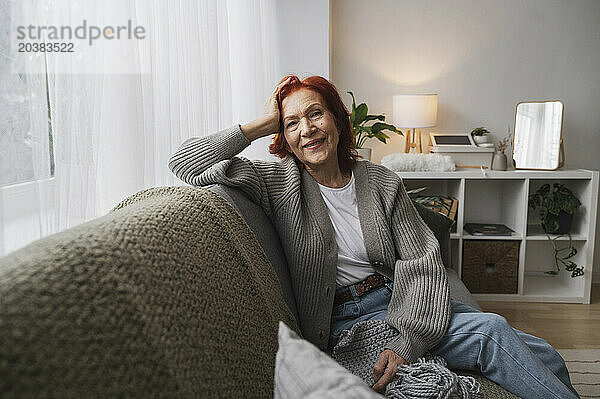 Smiling retired senior redhead woman sitting on couch at home