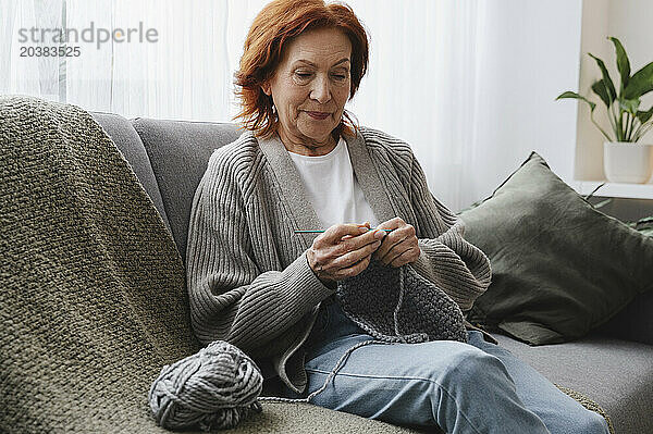 Retired redhead woman sitting on couch knitting at home