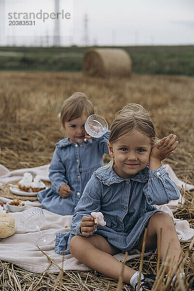 Smiling sisters spending leisure time sitting on picnic blanket