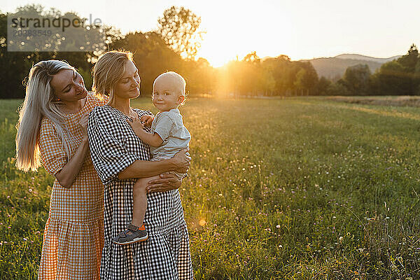 Mother carrying toddler standing with friend in park