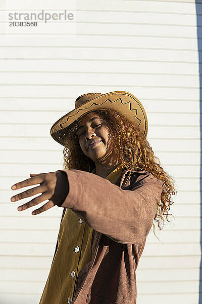 Smiling young woman with curly hair wearing jacket and cowboy hat