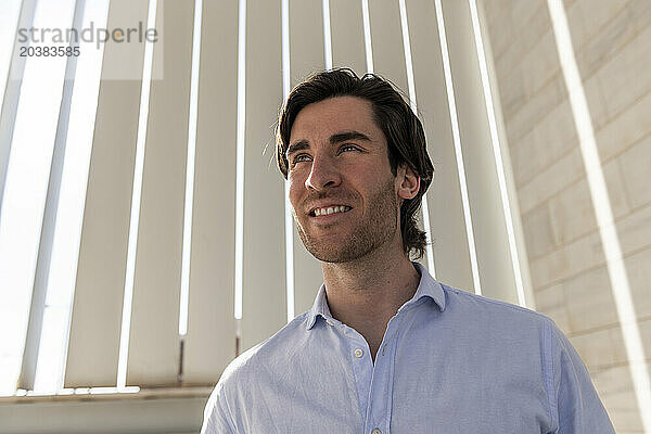 Thoughtful smiling young businessman in front of wall