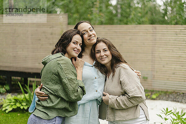 Smiling friends embracing together in back yard