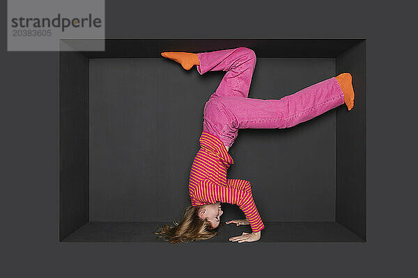 Teenage girl doing handstand over black background