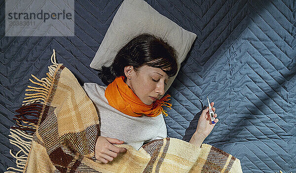 Woman holding thermometer and taking nap on bed at home