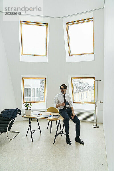 Businessman with coffee cup sitting at desk in minimalist office