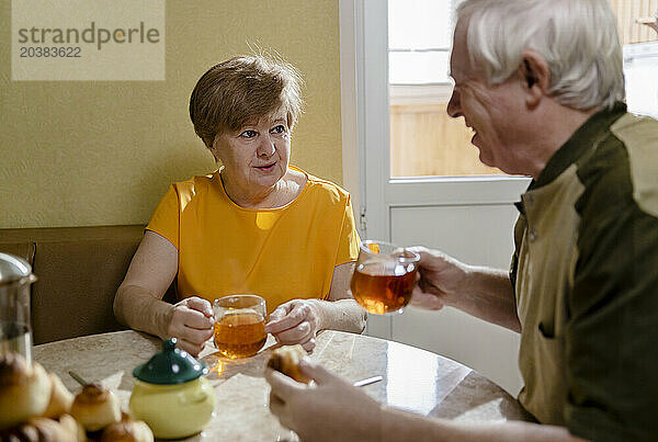 Smiling senior couple having cups of tea together at table