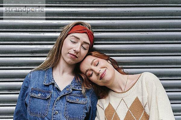 Smiling woman leaning on friends shoulder in front of shutter