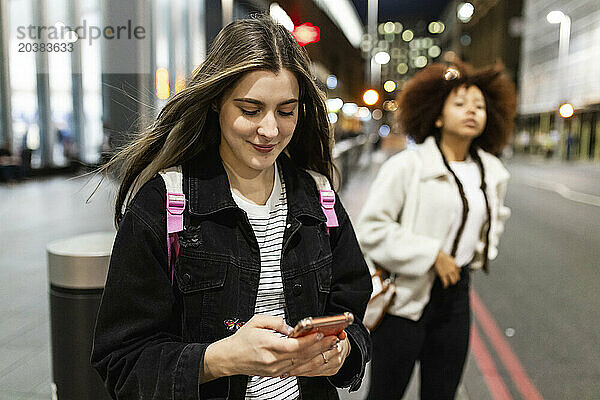 Smiling woman using smart phone with friend standing in background