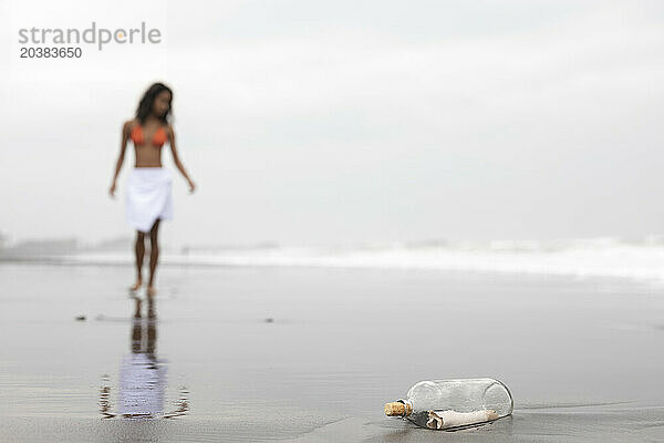 Message in glass bottle with woman on wet sand at beach
