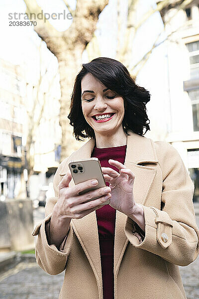 Smiling mature businesswoman wearing overcoat using smart phone