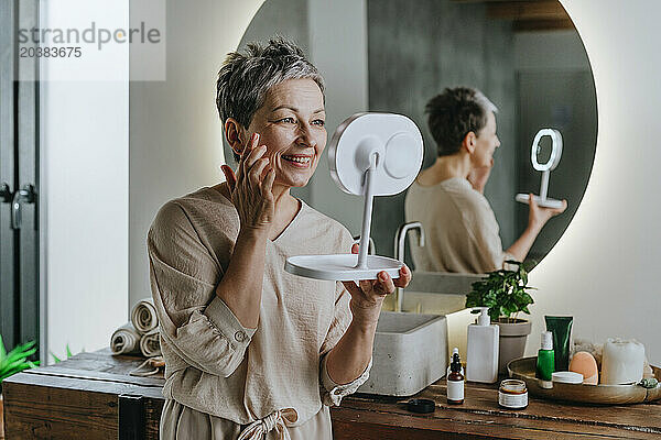 Smiling woman doing skin care looking in mirror at home