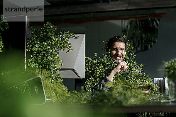 Happy businessman sitting amidst plants in office