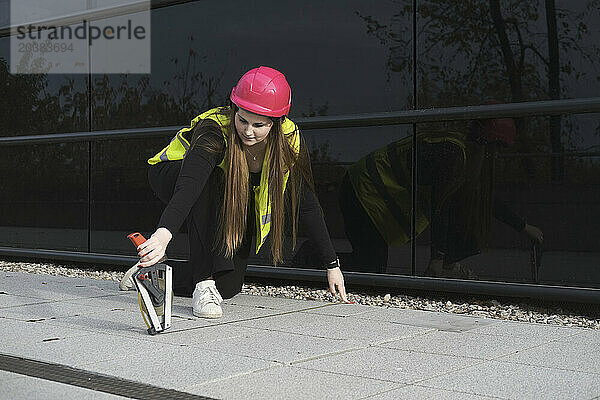 Young geodesist measuring floor width with tape near building