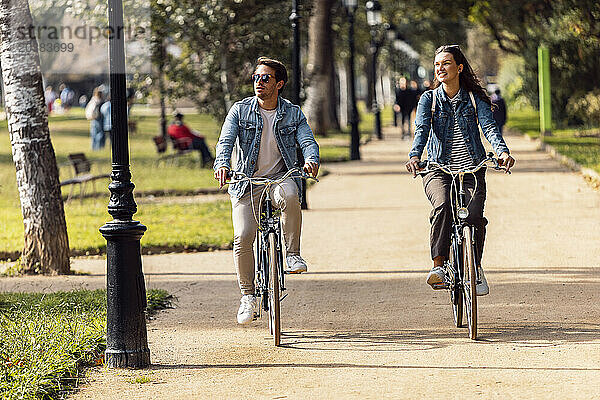 Smiling woman cycling with boyfriend on footpath in park