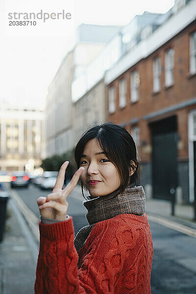 Young woman gesturing peace sign on street