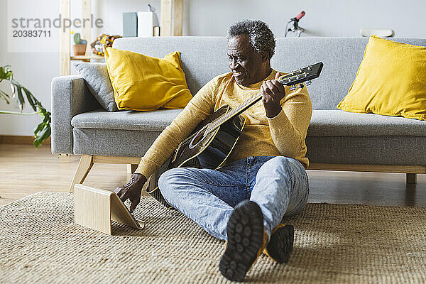 Happy senior man learning guitar online through tablet PC at home