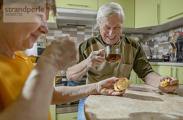 Happy senior man having sweet buns and tea together with woman at table