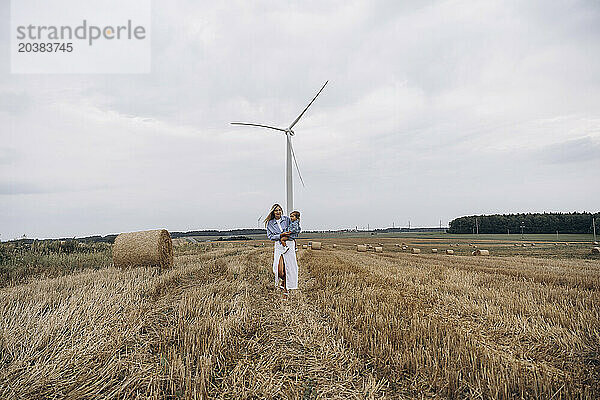 Woman carrying daughter and walking on hay at wind farm