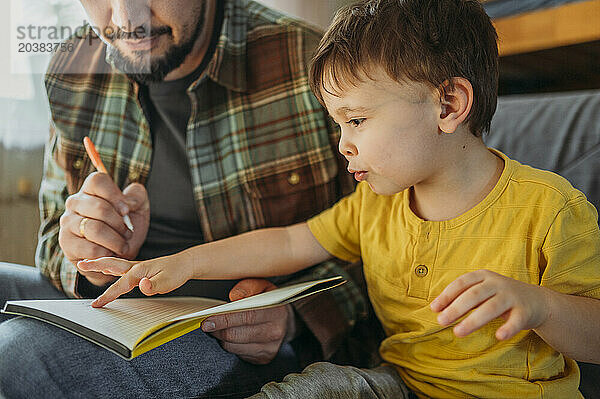 Father holding notepad and teaching son at home