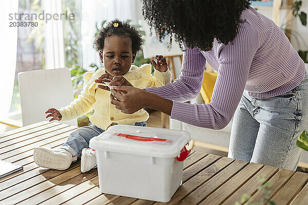 Single mother holding paper near daughter sitting by basket on wooden table at home