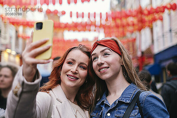 Happy friends taking selfie through smart phone in city