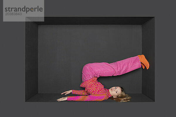 Teenage girl with legs up inside alcove by black background